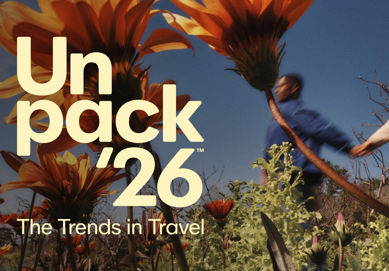People holding hands and walking past large orange flowers with a blue sky in the background. With "Unpack '26 The Trends in Travel" text over the image
