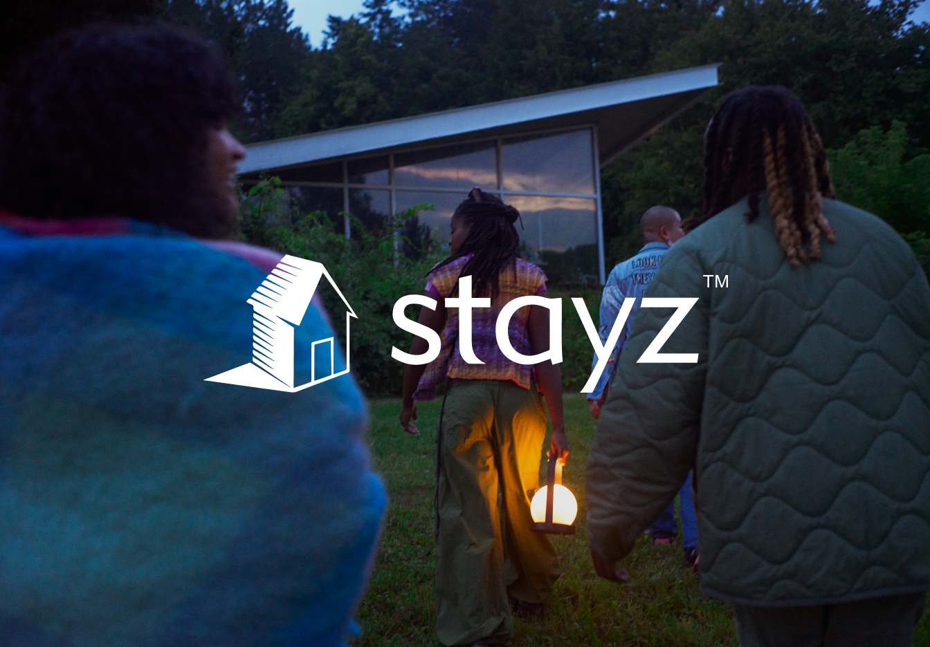 A group of people, one of them holding a lantern, walking towards a house. The Vrbo logo is displayed on top.