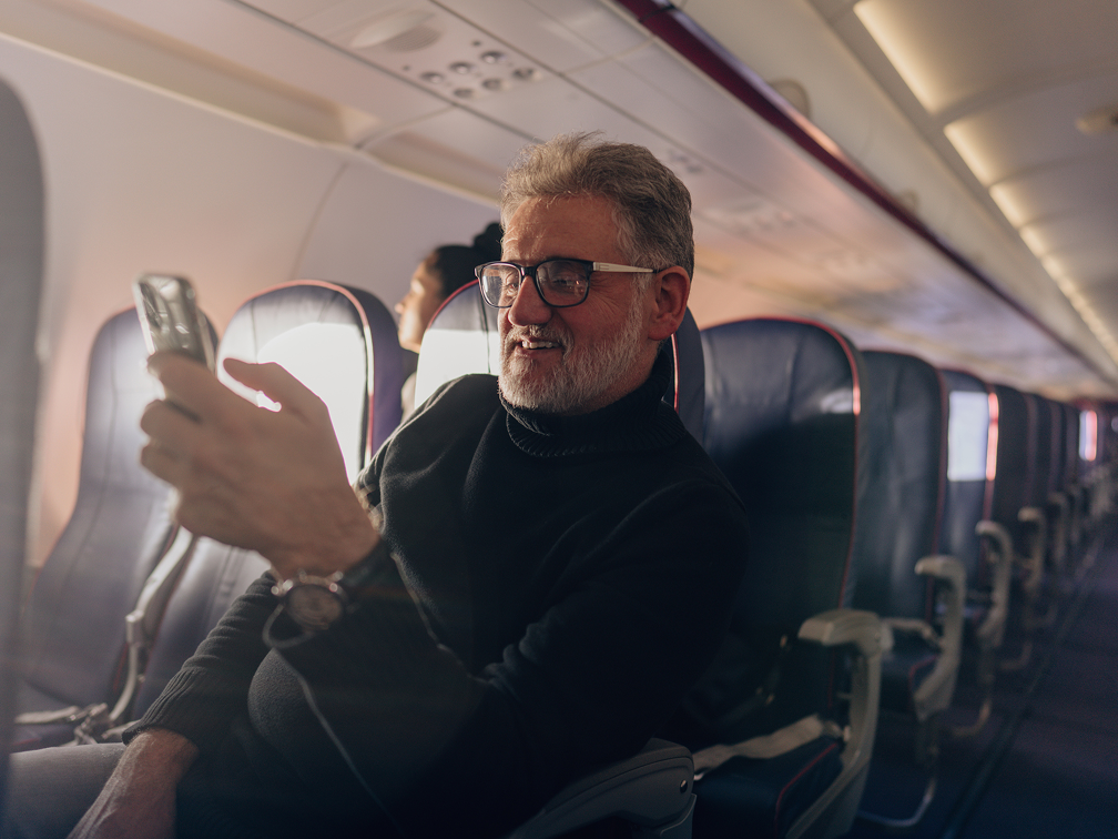 Man looking at a phone sitting inside of an airplane cabin.