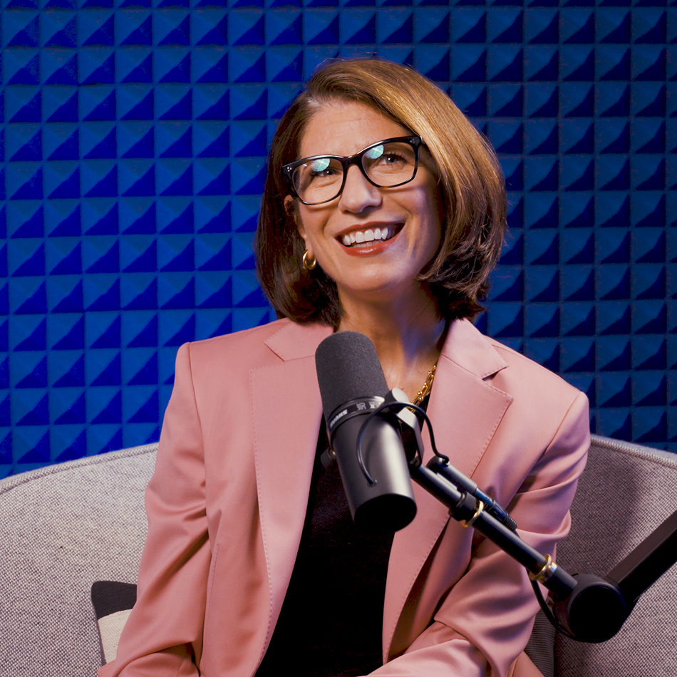 Ariane Gorin, CEO of Expedia Group, turned to her left in a profile view, smiling and speaking into a microphone in a blue soundproof studio