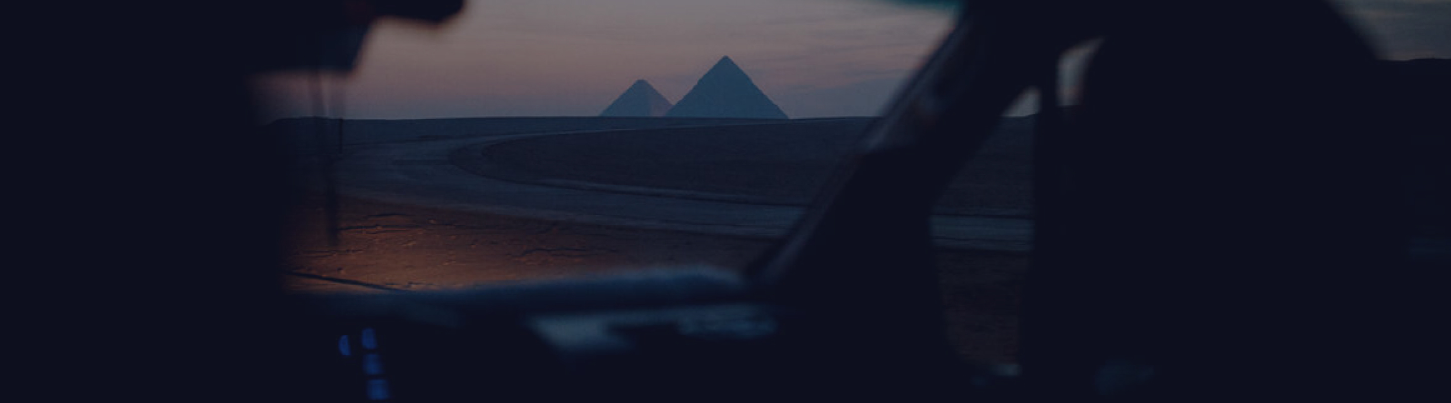 View of pyramids at sunset seen from inside a vehicle, with silhouetted dashboard framing the scene.