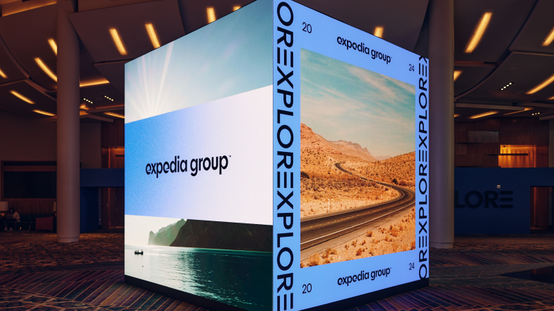 A large, modern-looking LED display cube showcasing Expedia Group EXPLORE branding in an event space.