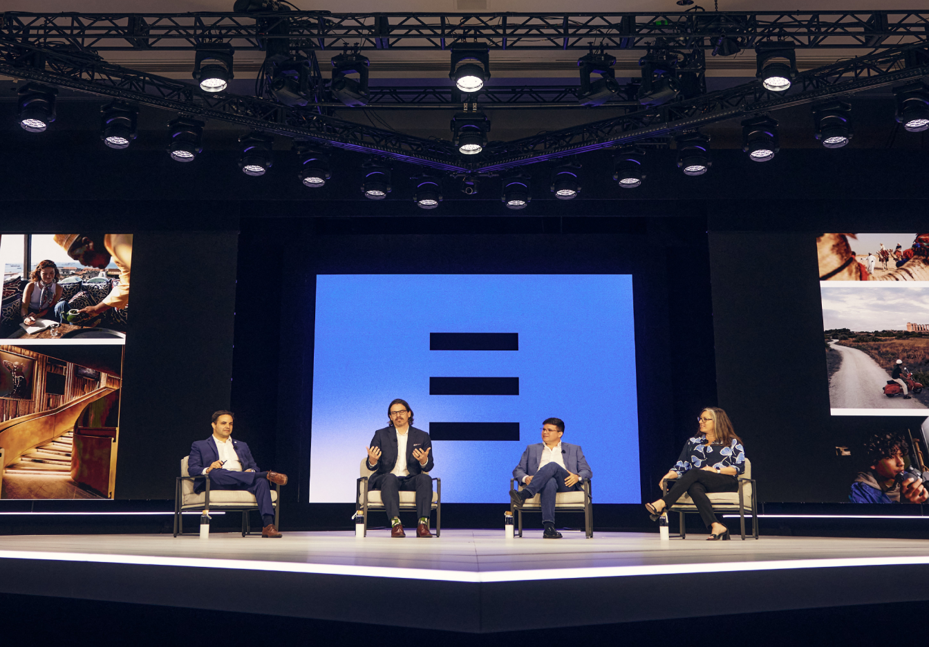 A panel discussion on a well-lit, modern stage, featuring four speakers seated in chairs with the Expedia Group EXPLORE logo on a display behind them.