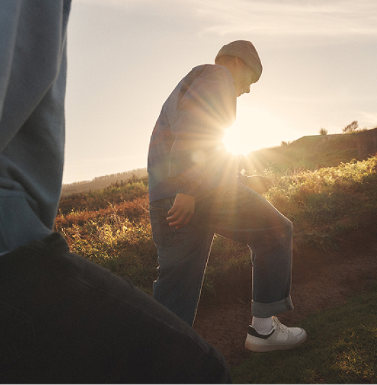 A group of friends walks through a scenic field at sunset with lens flare in the background.
