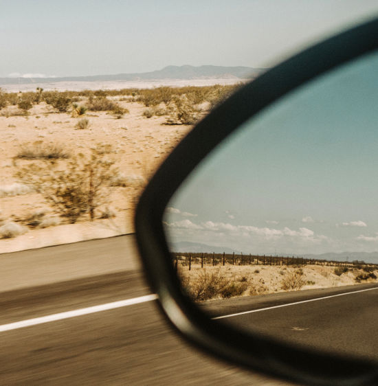 A close-up shot of a driver-side window showing an open desert road