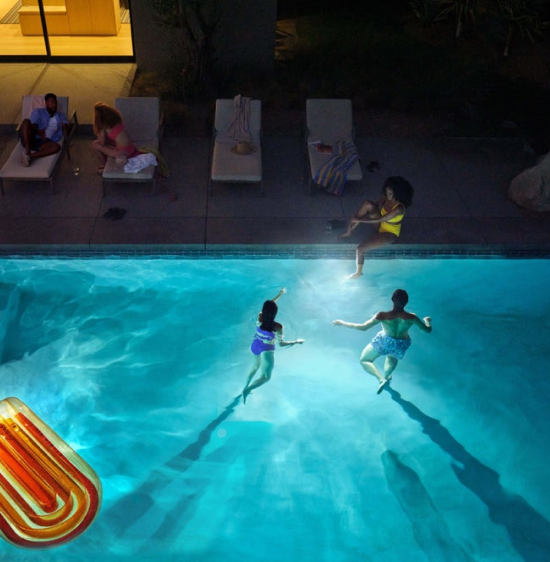 A group of people swimming in an illuminated pool at night