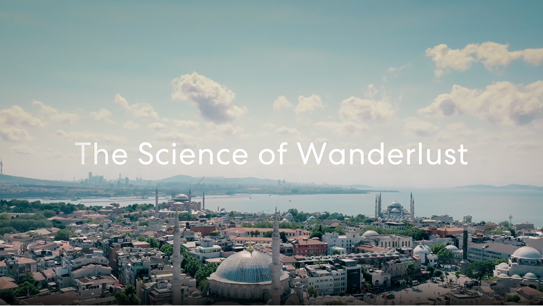  Vue aérienne d’une ville côtière avec des toits en dôme et des minarets sous un ciel partiellement nuageux, avec le texte « The Science of Wanderlust » (La science de l’envie de voyager), en surimpression sur l’image.