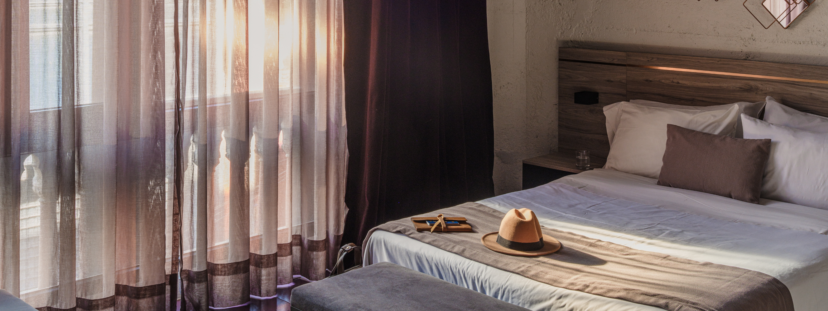 Photo of a sunlit hotel room with a hat on the bed.