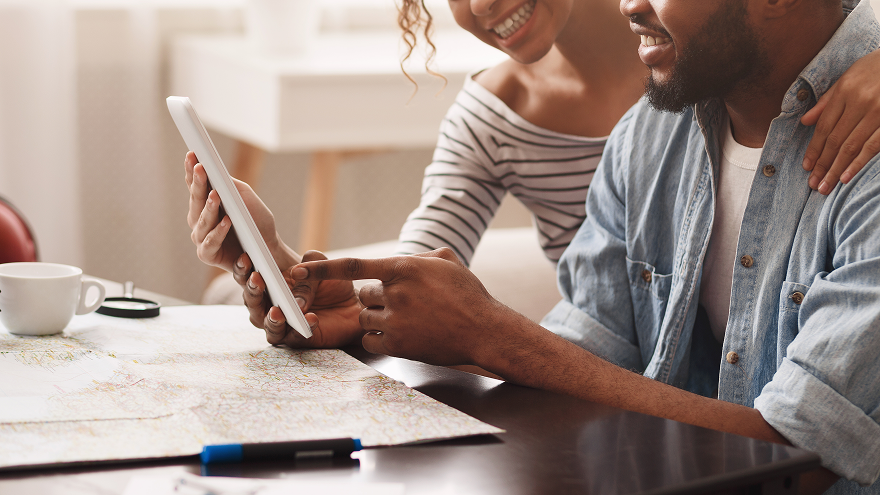 couple looking at a tablet while seated at a table with a map