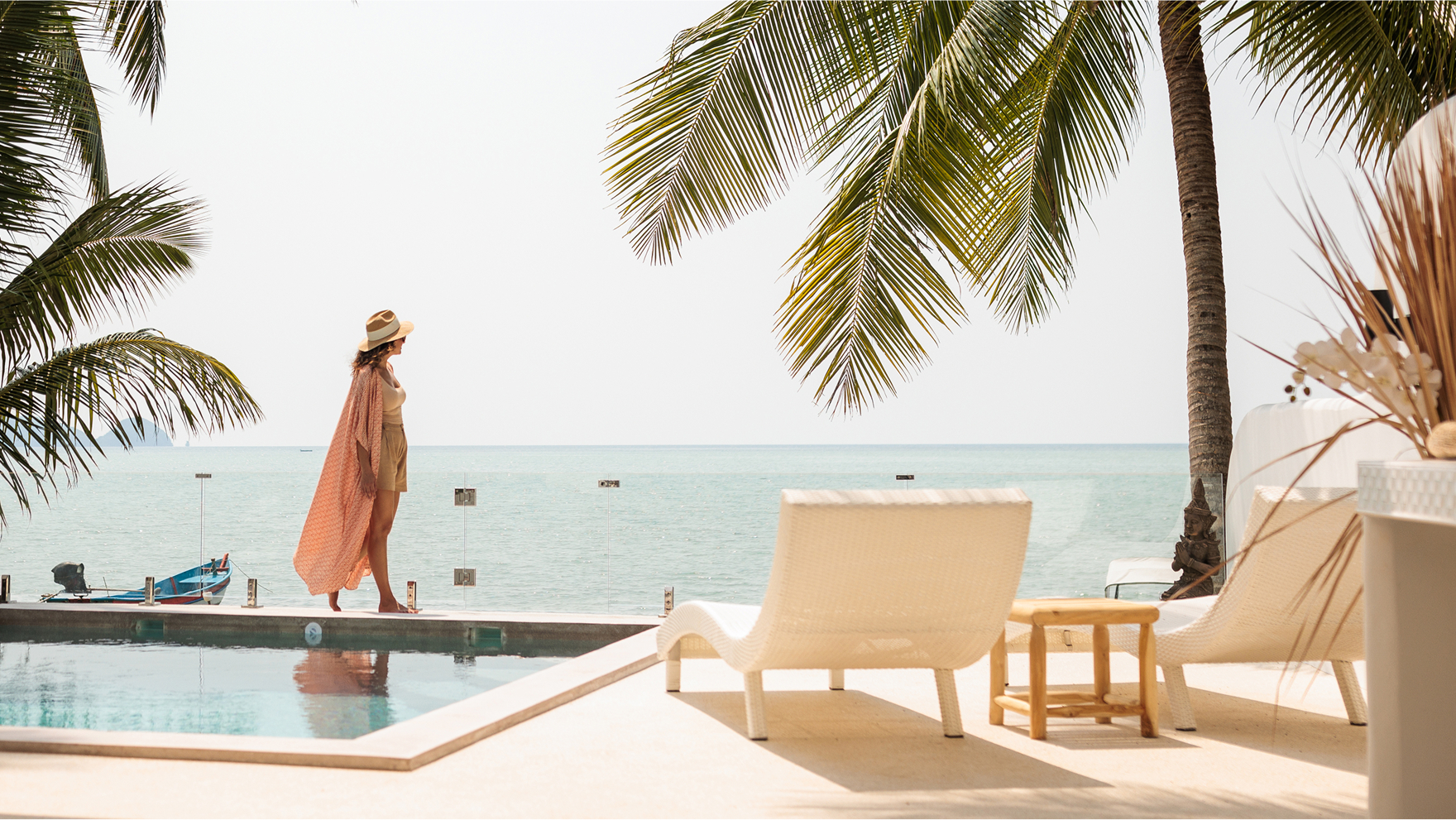 Woman walking along a tropical pool deck with ocean views and palm trees, evoking luxury travel inspiration.