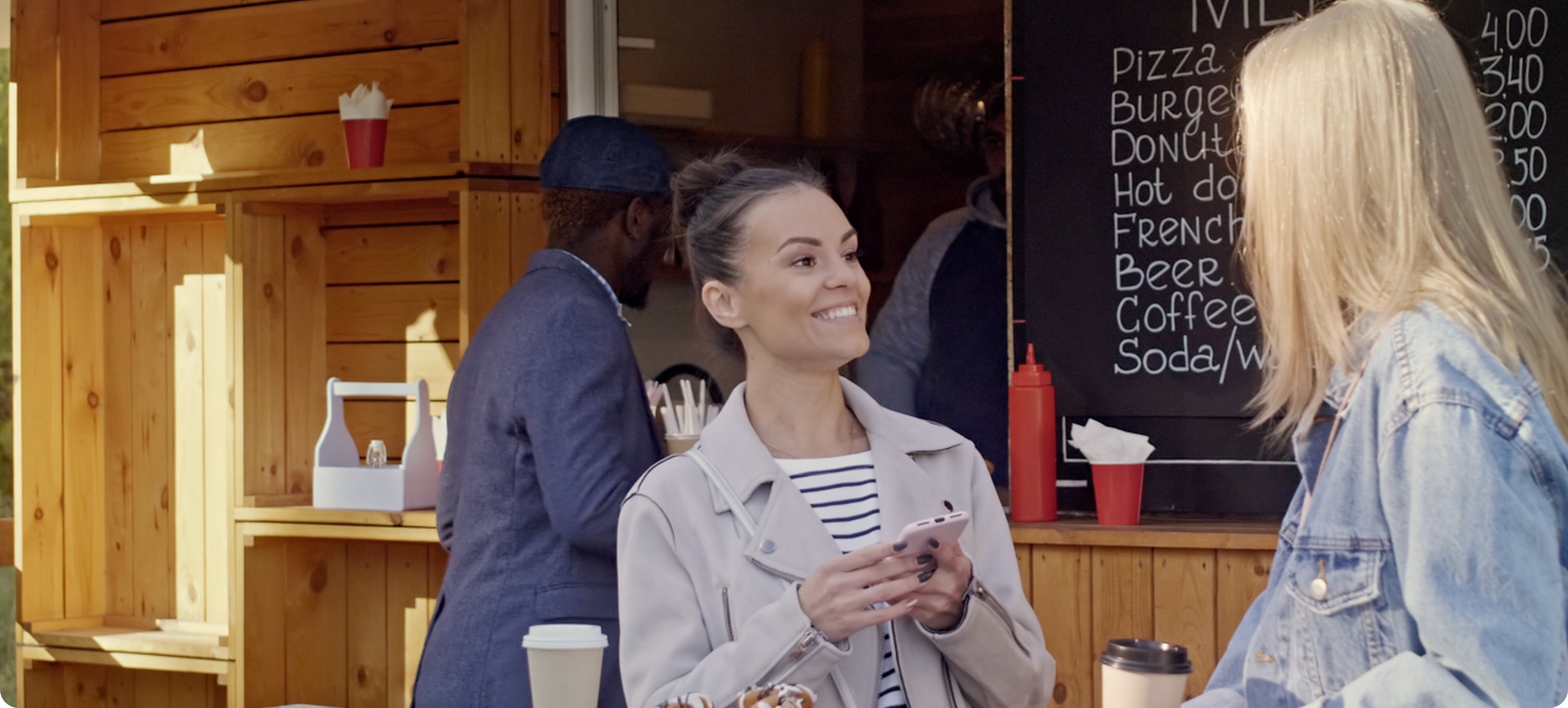 two women talking near coffee shop and looking at a smartphone.