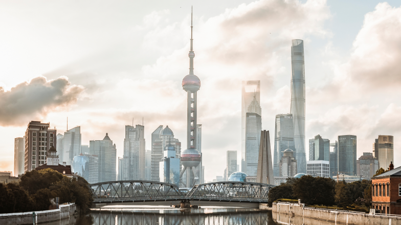 Shanghai's skyline at sunset, featuring the Oriental Pearl Tower and other modern skyscrapers with a view of the Huangpu River reflecting the skyline.