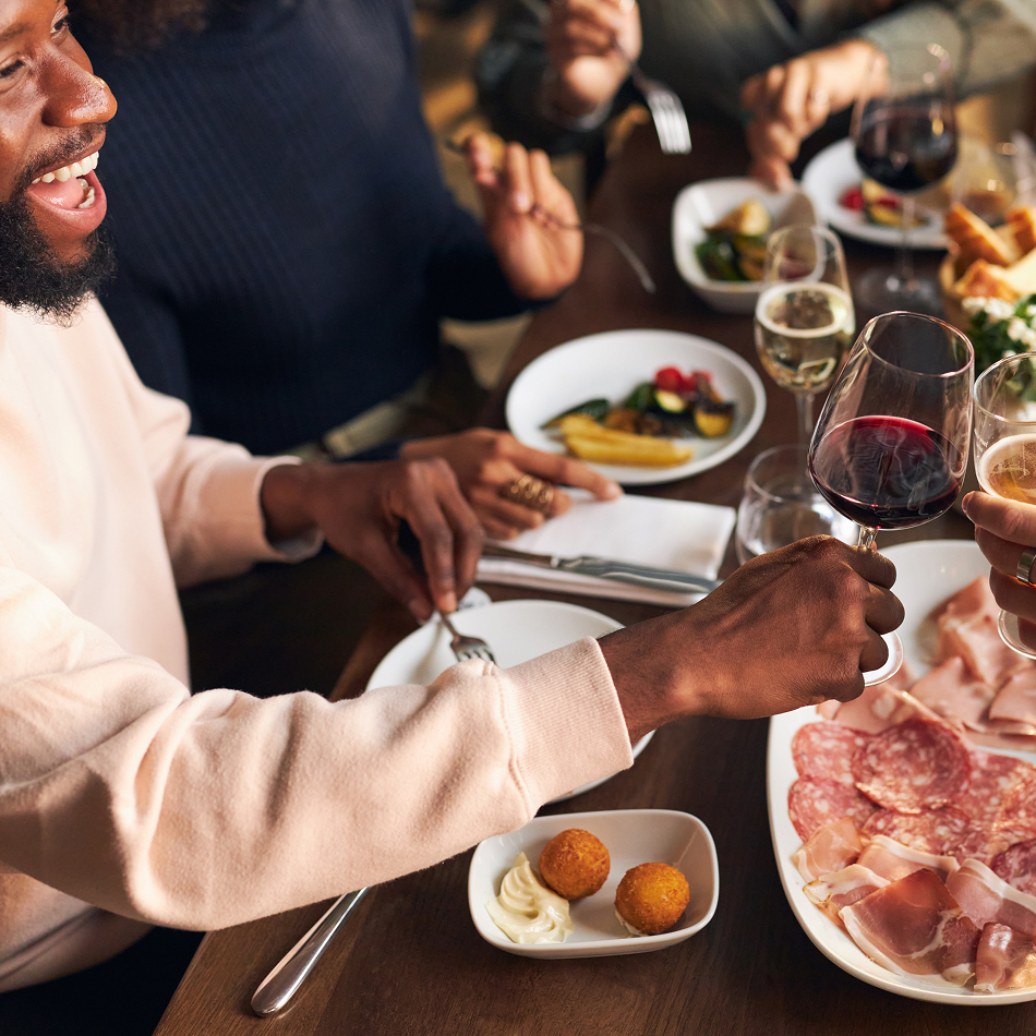 Group of friends dining together, raising glasses of wine over a table with charcuterie, small bites, and assorted plates