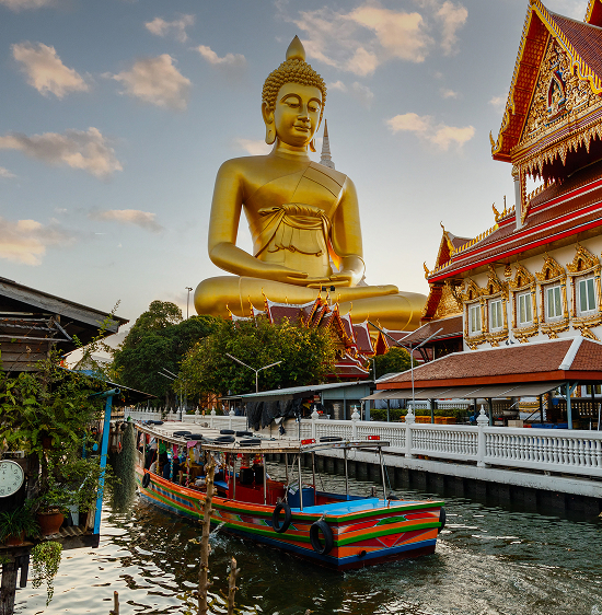  Large golden Buddha statue seen outdoors with greenery in the background.