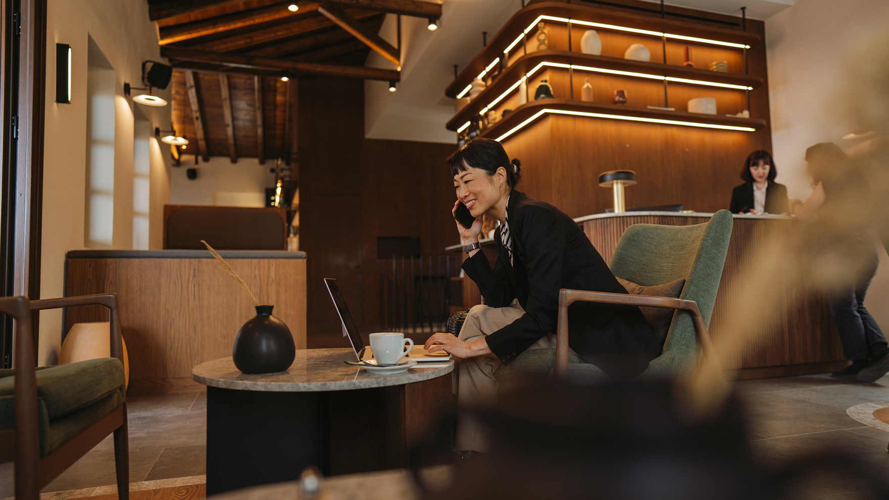 Guest sitting in a stylish hotel lobby working on a laptop with coffee on the table.