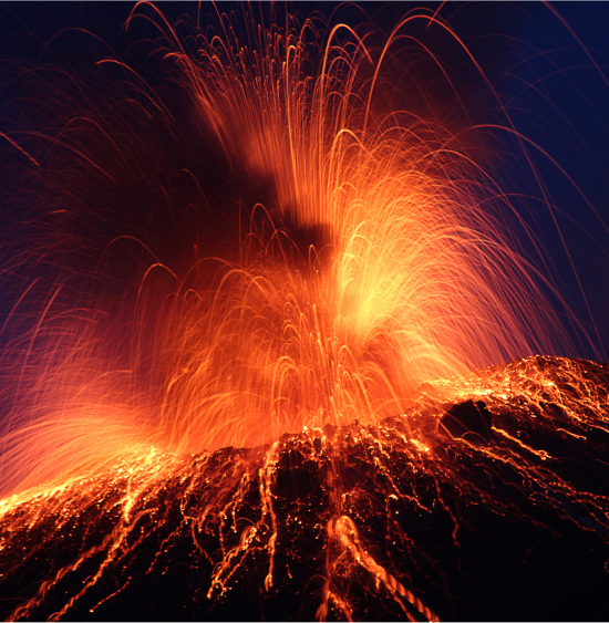 Close up photograph of the top of a volcano erupting with a night sky in the background.