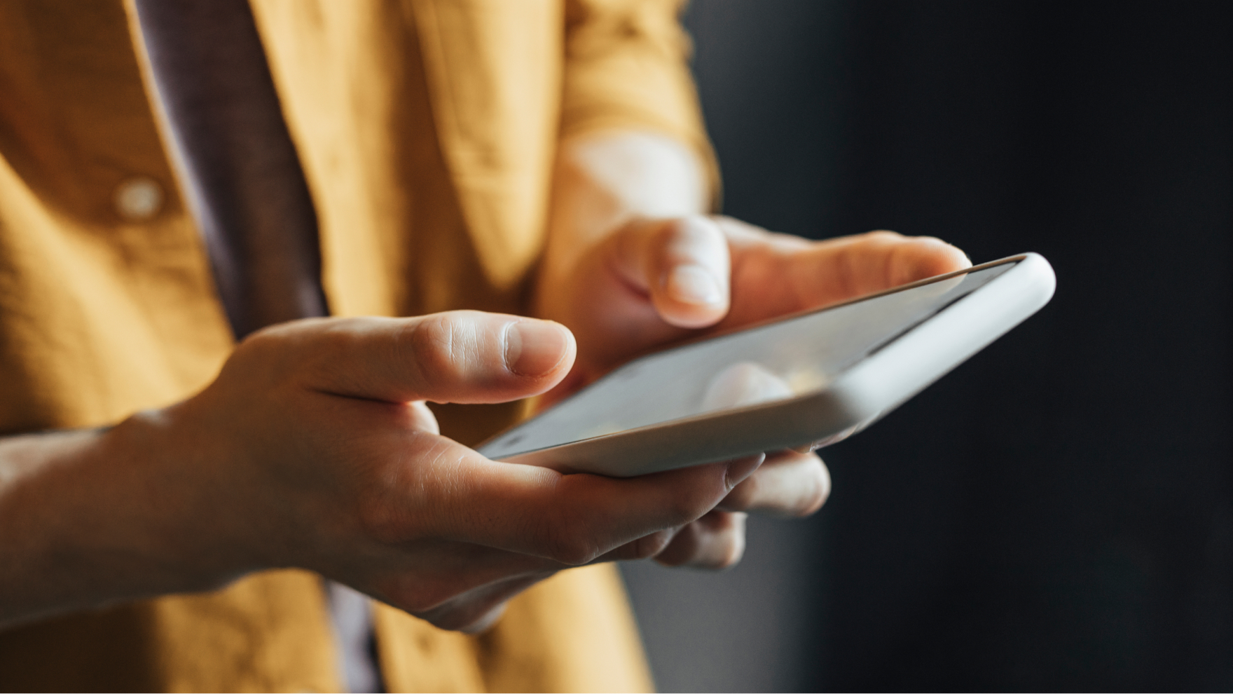 Person holding a phone device, wearing a mustard shirt in a softly lit environment