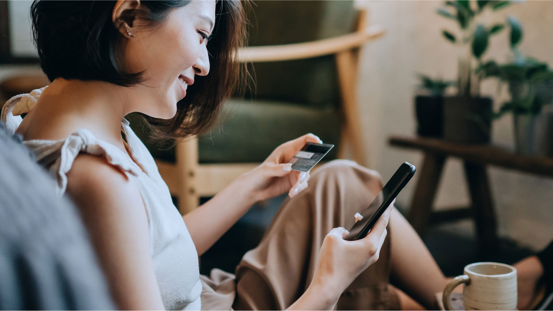 Person holding a credit card in one hand and using a smartphone with the other while sitting at a table