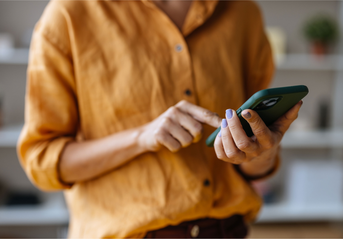 Person wearing an orange sweater using a smartphone with a blurred background in the background