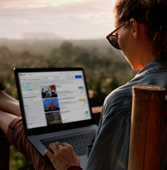 A woman works on her laptop on a wooden chair overlooking a misty city from a balcony.