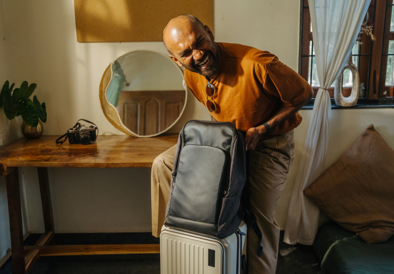 Traveler smiling while packing a backpack on top of a suitcase in a cozy room.