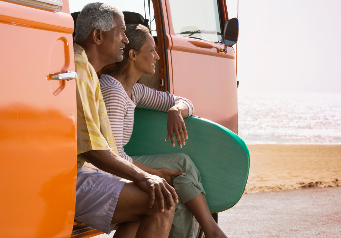 An older married couple enjoys the beach from their orange van.