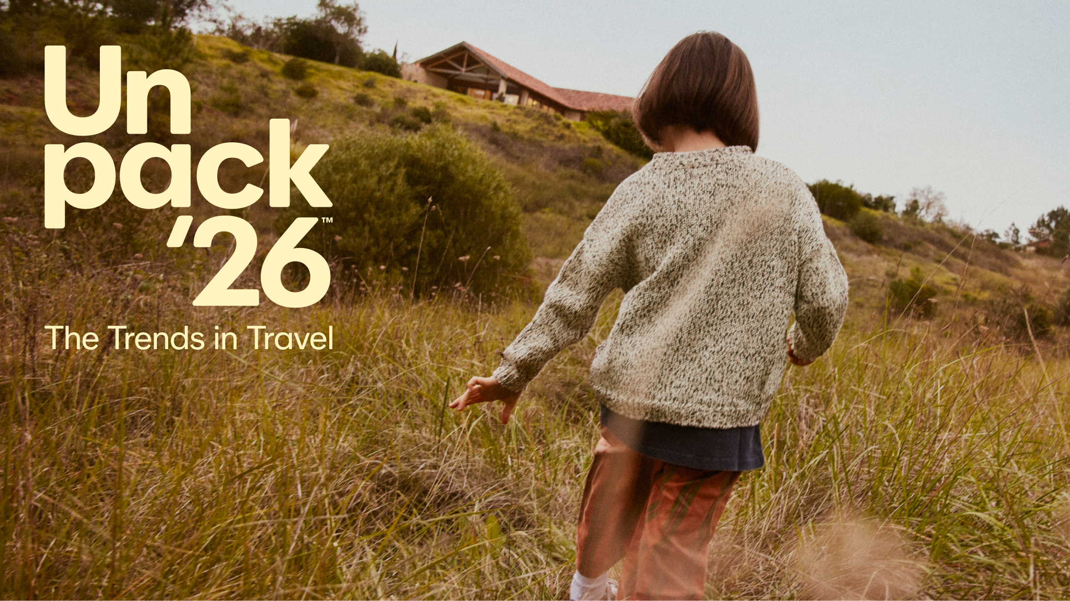Person wearing a sweater walking through tall grass, with large “Unpack ‘26 The Trends in Travel” text overlayed