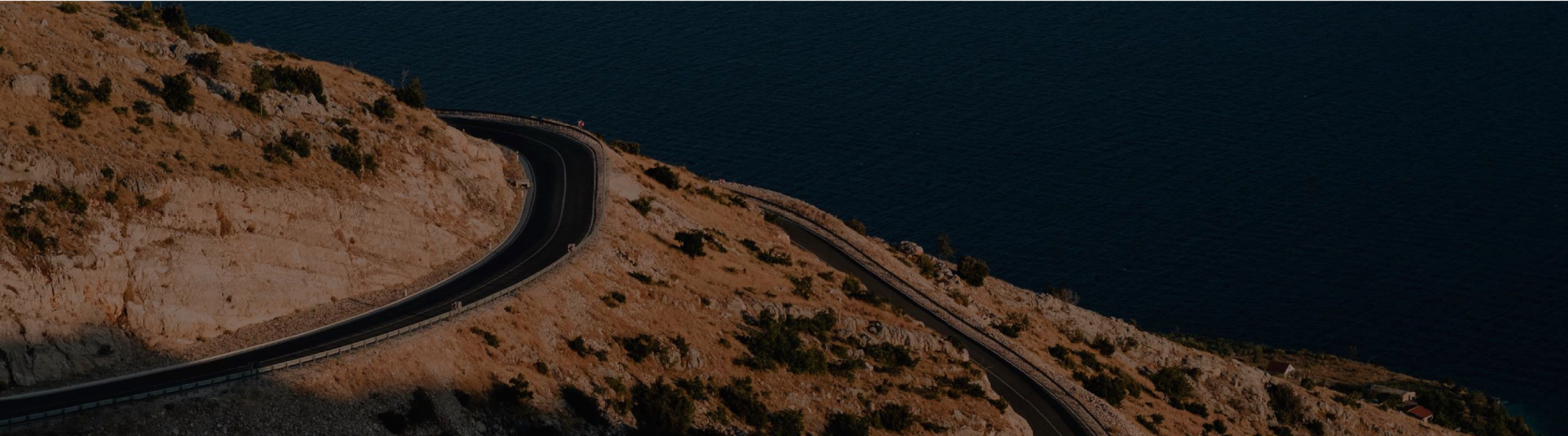 Una imagen de una sinuosa carretera que discurre entre una ladera rocosa y vistas al profundo mar azul.