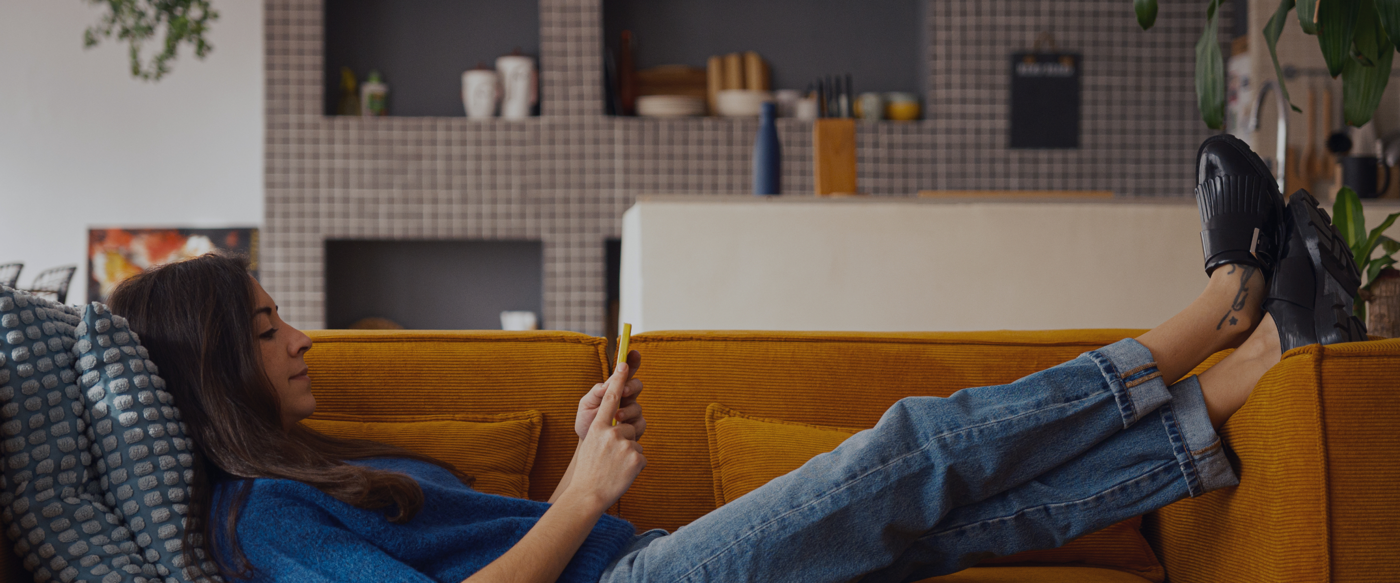 Woman lying on a mustard yellow couch browsing her phone in a modern living room